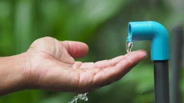 Su kaynakları kıtlığı kavramı. Adam musluğun altında ellerini yıkıyor ve su akıyor.