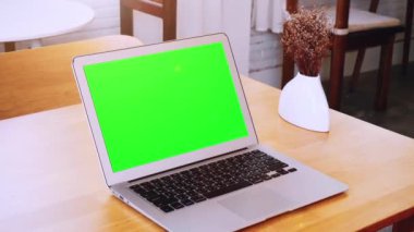 Tatilde bir kahve dükkanındaki ahşap bir masaya yerleştirilmiş yeşil ekran laptop..