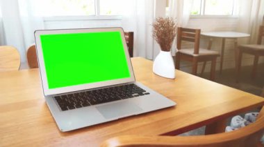 Tatilde bir kahve dükkanındaki ahşap bir masaya yerleştirilmiş yeşil ekran laptop..
