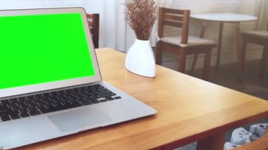 Tatilde bir kahve dükkanındaki ahşap bir masaya yerleştirilmiş yeşil ekran laptop..