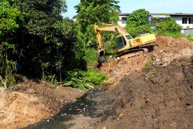 İnşaat alanında kazıcı. Yerdeki kazıcı. Kazıcı yağmur mevsiminden önce suyu boşaltmak için tıkalı kanallar kazıyor.