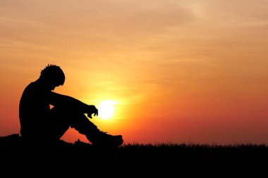 Bir adamın silueti çimenlerde oturuyor ve başka tarafa bakıyor.