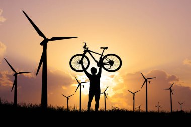 Gün batımında insan ve bisikletin silueti. Arka planda rüzgar türbinleri