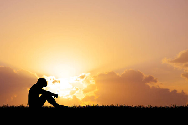 Силуэт человека, сидящего на траве и глядя на закат