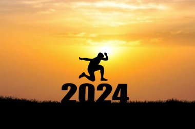 2024 'ün üzerinden atlayan bir adamın silueti. Gün batımında işaret ver. 