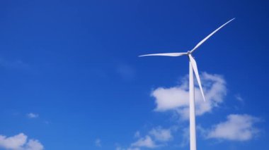 Rüzgar tarlası türbini mavi gökyüzünde dönüyor.