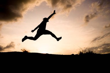 Arka planda dramatik bir günbatımı gökyüzü ile havaya sıçrayan bir kişinin silueti, özgürlüğü ve macerayı simgeliyor..