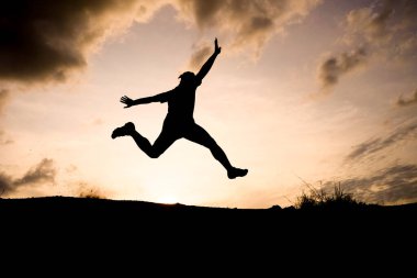 Gün batımında dramatik bir gökyüzüne doğru kollarını açmış zıplayan bir insanın silueti özgürlüğü ve macerayı simgeliyor..