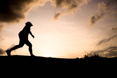 Gün batımında dramatik bulutlarla koşan bir insanın silueti, açık hava spor ve özgürlüğünü ön plana çıkarıyor..