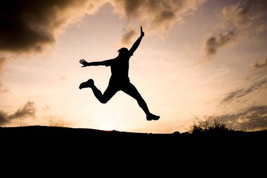 Havaya sıçrayan bir insanın silueti güzel bir günbatımı gökyüzüne doğru, özgürlüğü ve neşeyi simgeliyor..