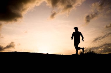 Gün batımında dramatik bulutlarla koşan bir koşucunun silueti, açık hava fitnesini ve doğanın güzelliğini yakalıyor..