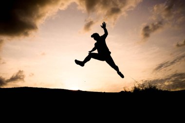 Gün batımında dramatik bir gökyüzüne doğru atlayan bir insanın silueti özgürlük ve macerayı simgeliyor..