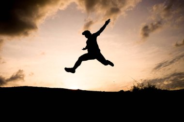 Havaya sıçrayan dinamik bir siluet güzel bir günbatımına karşı, özgürlüğü ve macerayı simgeliyor..