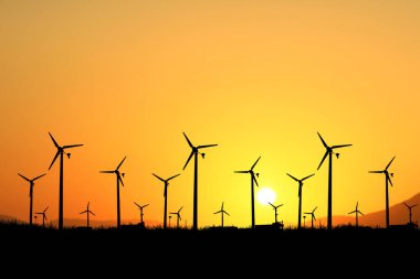 Siluetli rüzgar türbinleri canlı turuncu bir gün batımına karşı, yenilenebilir enerji ve manzaranın sürdürülebilir gücünü vurguluyor..