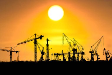 Siluetli vinçler canlı bir günbatımına karşı dimdik ayakta durarak çarpıcı bir sanayi manzarası yaratıyor..