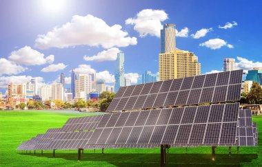 Güneş panelleri yeşil bir alanda modern bir şehrin arka planında gökyüzü açık mavi gökyüzü ve beyaz bulutların olduğu güneşli bir günde.