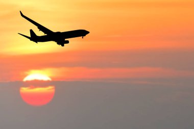 Bir uçağın silueti canlı bir günbatımı gökyüzüne karşı uçuyor ve arka planda parlayan bir güneş var..