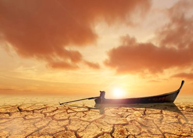 Çatlamış, kuru bir yerde, iklim değişikliğini, kuraklığı ve çevresel zorlukları sembolize eden, dramatik bir gün batımı gökyüzü olan yalnız bir tekne..