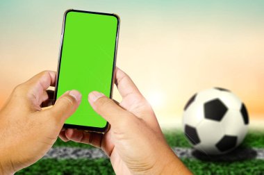 Spor ve teknoloji temaları için ideal olan, gün batımında çimen tarlasında yeşil ekranlı akıllı telefonu tutan eller..