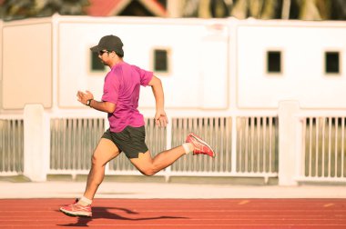 Pembe bir gömlek ve siyah şort giymiş, parlak güneş ışığında koşan sporcu, hız ve zindelik gösteriyor..