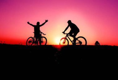 İki siluetli bisikletçi serüvenin ve özgürlüğün özünü yakalayan çarpıcı bir günbatımı arka planına doğru yol alıyorlar..