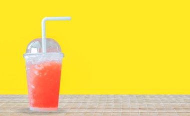 Net bir plastik bardakta, parlak sarı arkaplanlı, dokunmuş bir paspasın üzerine yerleştirilmiş canlı kırmızı bir içecek..