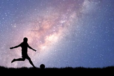 Samanyolu Galaksisi ile büyüleyici bir yıldızlı gökyüzü altında futbol oynayan bir kişinin silueti.