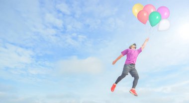 Pembe gömlekli ve kırmızı ayakkabılı bir adam gökyüzünde süzülüyor, parlak, güneşli bir günün arka planına renkli balonlar tutuyor, dağınık bulutlu..