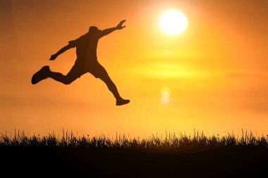 Göz kamaştırıcı bir gün batımında, ön planda güneş ve çimlerle havaya sıçrayan bir insanın silueti..