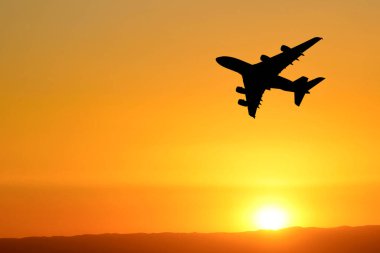 Canlı turuncu bir gün batımına karşı silueti olan uçak, seyahat ve macerayı simgeliyor..