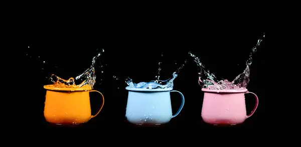 stock image Three colorful mugs with splashing water captured against a black background, showcasing vibrant energy and motion.