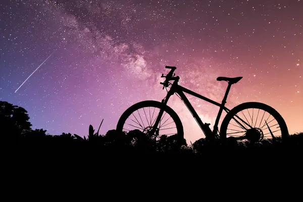stock image A stunning silhouette of a bicycle set against a vibrant, starry night sky featuring a shooting star and the Milky Way.