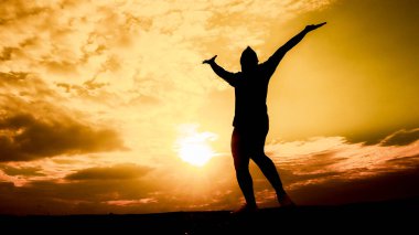 Canlı, altın bir günbatımı gökyüzüne karşı kollarını kaldırmış özgürlük ve neşeyi simgeleyen bir insan silueti..