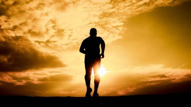 Çarpıcı bir günbatımı arkaplanına doğru koşan bir adamın silüeti dramatik bulutlar ve altın ışıkla.