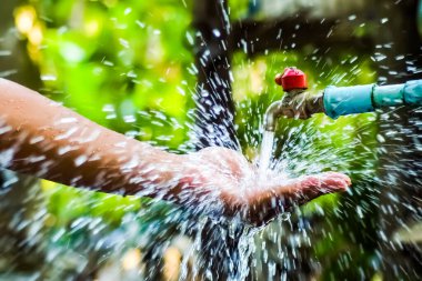 Musluktan fışkıran suyun yakın plan görüntüsü canlı bir bahçede bir ele sıçrayıp tazeliğin ve doğanın özünü yakalıyor..