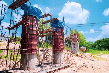 Yapı iskelesi ve beton sütunlarla kaplı, parlak mavi gökyüzüne karşı kabarık bulutlarla kaplı..