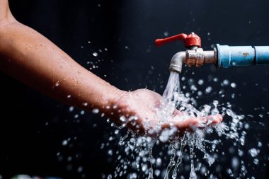 Akan bir musluğun altında yıkanan bir elin detaylı görüntüsü, su sıçramalarını ve hijyen sorunlarını vurguluyor..