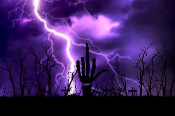 stock image Eerie graveyard scene with a skeleton hand emerging from the ground, surrounded by leafless trees and lightning in the night sky.