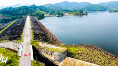 Etrafındaki yemyeşil tepelerin ve dağların doğal güzelliğini gösteren bir baraj ve su deposunun nefes kesici hava manzarası..