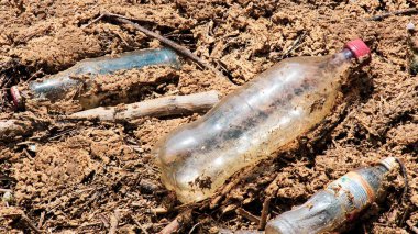 Çamurlu bir ortamda plastik şişe ve molozların yakın planda tutulması, kirlilik ve çevresel kaygıların vurgulanması.