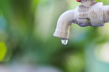 Su damlacığıyla su musluğunun detaylı bir yakın plan görüntüsü, yeşil bulanık arkaplan üzerine kurulmuş, suyun korunmasını vurguluyor.