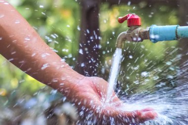 Açık hava musluğunun altında her yöne su sıçrayan bir elin yakın plan görüntüsü..
