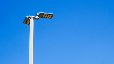 Modern bir sokak lambasının minimalist bir görüntüsü canlı, berrak bir mavi gökyüzüne karşı kurulmuş, kentsel basitliğin ve çağdaş tasarımın özünü yakalıyor..