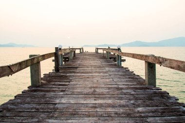 Sakin sulara uzanan sakin bir ahşap iskele manzarası, sakin bir gün doğumu ve arka planda uzak dağlar..