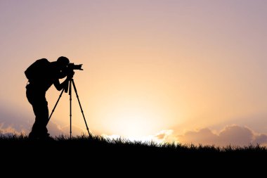 Bir fotoğrafçının silueti güzel bir gün batımında üç ayaklı bir kamerayla fotoğraf çekiyor..