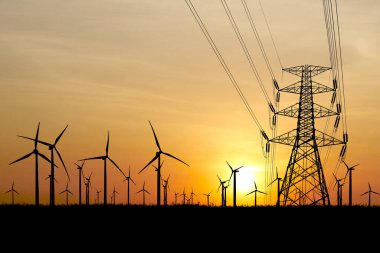 Siluetli rüzgar türbinleri ve elektrik hatları canlı bir günbatımı gökyüzüne karşı, yenilenebilir enerji ve kırpma yolu ile çevre temaları için mükemmel.
