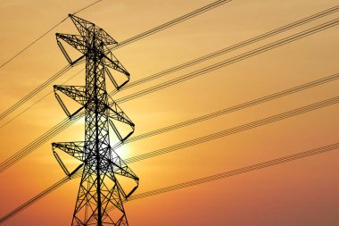 Yüksek voltaj iletim kulesinin silüeti çarpıcı turuncu gün batımı gökyüzüne karşı elektrik hatlarıyla çevrili..