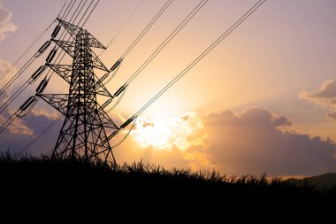 Yüksek voltajlı elektrik hatlarının silueti ve arka planda dramatik bir günbatımı gökyüzü olan kule enerji ve altyapı sergiliyor..