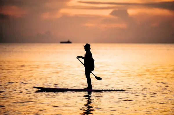 stock image A serene scene of a person paddleboarding during a beautiful sunset, with calm ocean waters and a ship visible in the background.