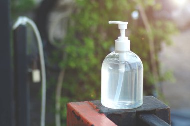 Temiz bir el dezenfektanı şişesi, arka planda yeşil yeşillikler bulunan ahşap bir yüzeye yerleştirilmiş..